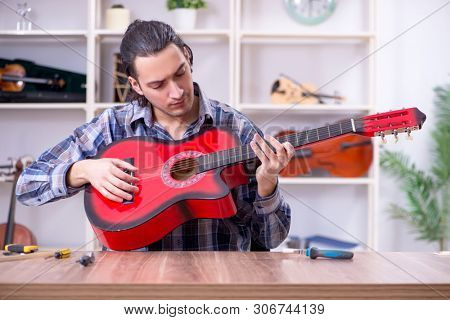 Young handsome repairman repairing guitar