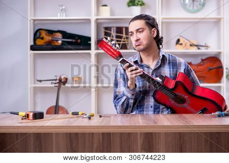 Young handsome repairman repairing guitar