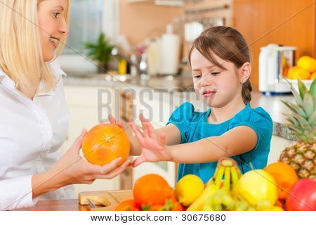 Healthy eating - mother and child sitting in the kitchen with different kinds of fruits, the kid doesnt like fruits for breakfast food