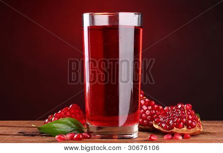 rijpe pomergranate en glas sap op houten tafel op rode achtergrond