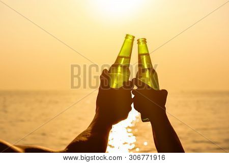Couple Hands Holding Beer Bottles Clanging And Celebrating On Holiday At The Beach In Summer Sunset