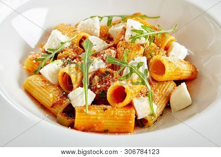 Exquisite Serving White Restaurant Plate of Homemade Rigatoni in Tomato Sauce with Milk Mozzarella. Stylish High Kitchen Italian Penne Pasta Tubes on Natural Black Marble Background