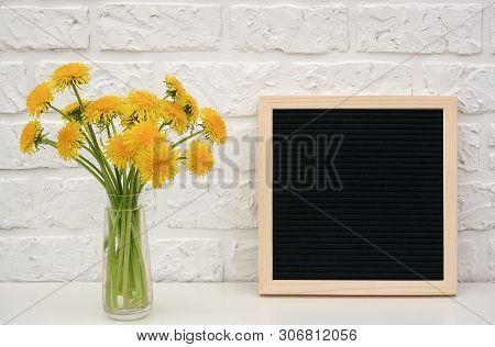 Bouquet Yellow Dandelion In Vase And Blank Black Letter Board On Table Against White Brick Wall. Moc