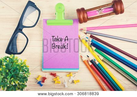 Woking Table With Hourglass, Pencils, Eyeglass And Take A Break Word Written On Notepad