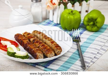 Kupaty In A White Plate And Vegetables On A Wooden Table. Sausages Grill. Tasty Food.