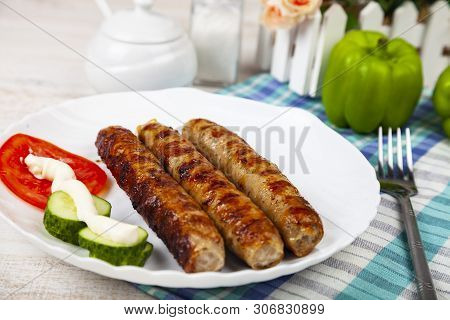 Kupaty In A White Plate And Vegetables On A Wooden Table. Sausages Grill. Tasty Food.