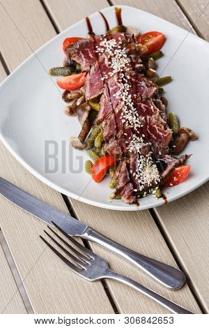 Sliced Medium Rare Roast Beef With Pickles, Cherry Tomatoes, Mushrooms On A White Plate On Wooden Ba