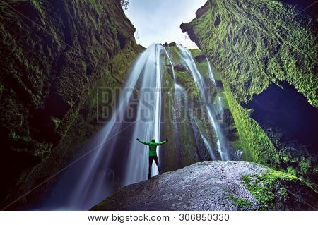 Man standing with hands up in the air in front of Gljufrafoss waterfall, Iceland. Concept of strength and victory.