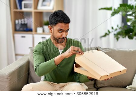 food delivery, consumption and people concept - excited indian man looking inside of takeaway pizza box at home