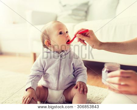 family, food, child, eating and parenthood concept - mother with puree and spoon feeding little baby at home