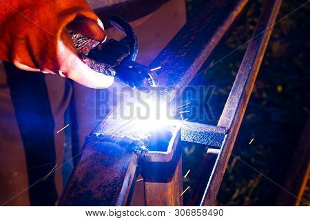 Welder Worker Performs Jump Welding. Man Welder In Protective Gloves Performs Arc-welding Process Of
