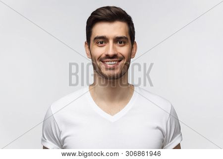 Portrait Of Smiling Handsome Young Man In White T-shirt Looking At Camera, Isolated On Gray Backgrou