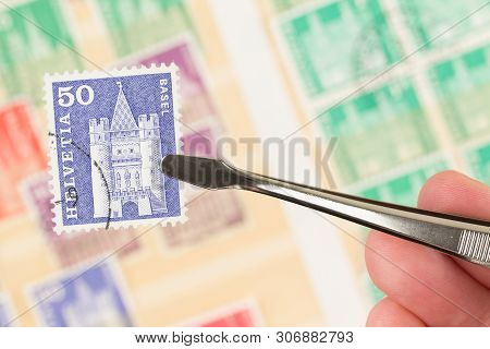 Seattle, Washington- May 29, 2019:  Hand Holding Tongs And Postage Stamp Are In Focus,  With Blurred