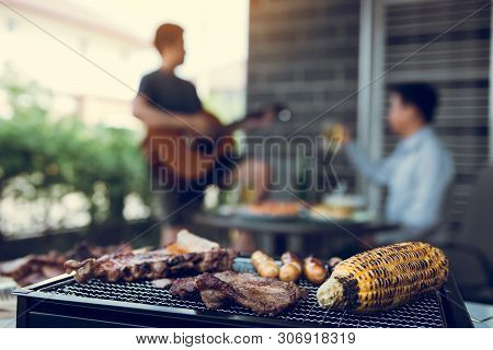 Close Up Grilled Meats And Various Food On The Grill And Celebrations Of Friends Who Are Playing Gui