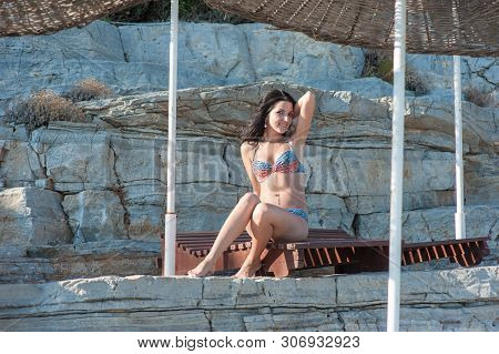 A Beautiful Brunette Sits On A Lounger. Young Girl In Sexy Bikini