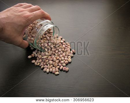 Pinto Bean Seeds Hand Dish.pinto Bean Seeds Are Poured From A Glass Jar On Brown Wooden Surface.clos