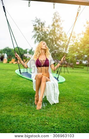 Youmg Beautiful Woman In Beautiful Summer Garden Is Round Swing