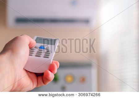 Male Hand With Air Conditioner Remote Control. The Man Switches The Air Conditioning Modes. Adjusts 