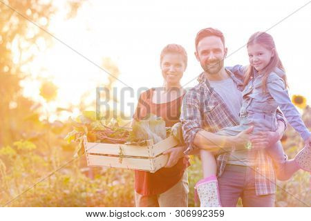 Portrait of smiling family with vegetables in crate at farm