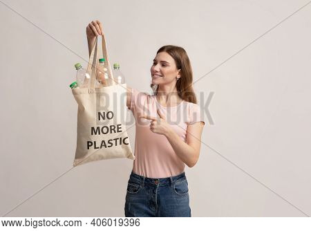 No More Plastic. Smiling Millennial Woman Pointing At Canvas Eco Tote Bag Filled With Empty Bottles 