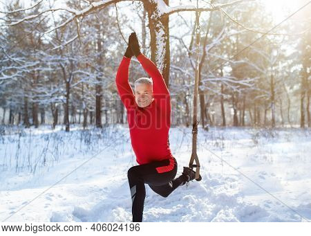 Outdoor Winter Fitness Concept. Sporty Senior Man Training With Trx Resistance Straps At Snowy Fores