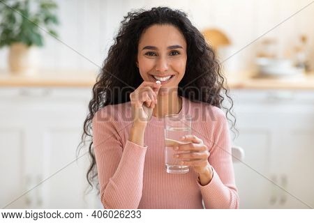 Beauty Supplement. Smiling Brunette Woman Taking Vitamin Pill And Drinking Water At Home, Attractive