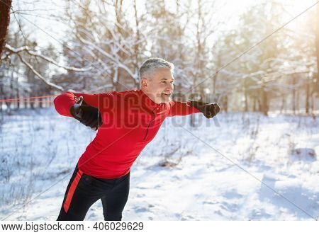 Winter Sports Concept. Handsome Senior Man Training With Fitness Straps At Snowy Forest, Copy Space.