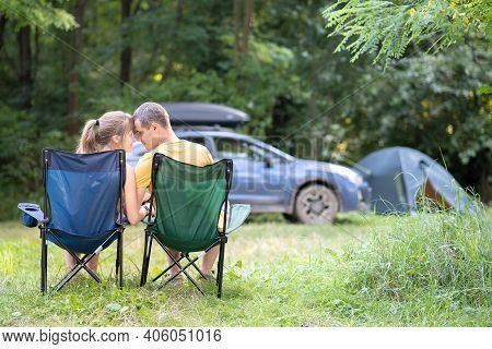 Happy Couple Sitting On Chairs At Campsite Hugging Each Other. Travel, Camping And Vacations Concept