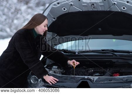 Woman checks the oil in the engine of the car in winter weather. Preparing the car for winter driving