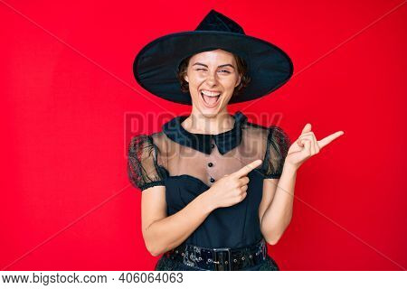 Young hispanic woman wearing witch halloween costume smiling and looking at the camera pointing with two hands and fingers to the side. 