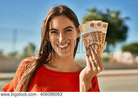 Young hispanic woman smiling happy holding hungarian forint banknotes at the city.