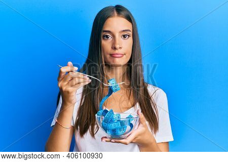 Young hispanic woman eating measure meter doing diet for weight loss relaxed with serious expression on face. simple and natural looking at the camera. 