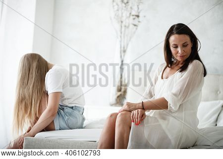 Family conflict and relations concept. Mother and daughter having quarrel and aguring at home. Sad woman and teenage girl sitting on bed. Not looking at each other.