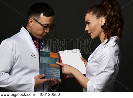 Young Woman And Man Doctors In White Medical Uniform Gown Discuss Professional Books With Blank Cove