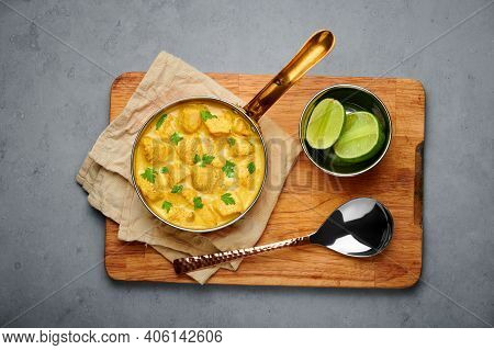 Chicken Korma In Copper Pan On Gray Concrete Table Top. Indian Cuisine Meat Curry Dish With Coconut