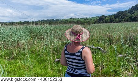 Caucasian Mature Woman Wearing Summer Hat Rear Unidentified Explores Overlooking  River Lagoon Wetla