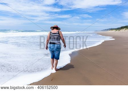 Caucasian Mature Woman Holidays Walking Beach Ocean Shoreline With Wave Foam Wash Onto Her Feet A Re