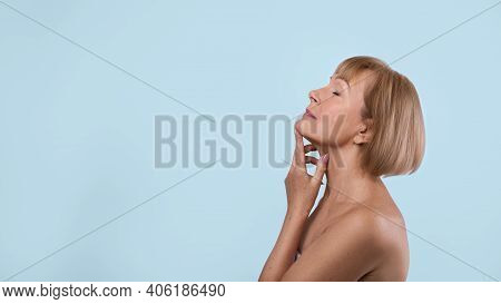 Graceful Aging Concept. Beautiful Senior Lady Touching Skin On Her Neck Over Blue Studio Background.