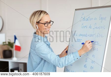 Friendly Female Teacher Writing Grammar Rules On Blackboard During Online French Lesson. Positive Yo