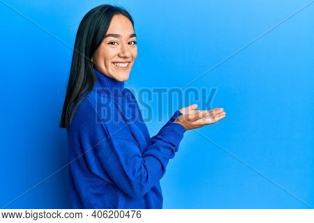 Young asian woman wearing casual winter sweater pointing aside with hands open palms showing copy space, presenting advertisement smiling excited happy 