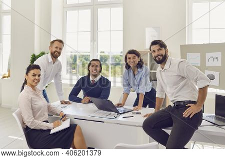 Group Of Young Smiling Business People Sitting In Office And Looking At Camera During Startup Discus