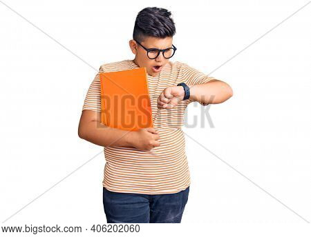 Little boy kid holding book wearing glasses looking at the watch time worried, afraid of getting late 