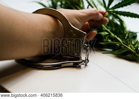 Marijuana Is Illegal. Hand In Handcuffs Against The Background Of Leaves Marijuana. Drug Dealer Unde