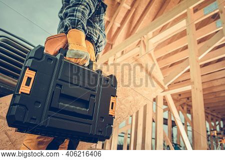 Construction Contractor With Plastic Power Tools Box In His Hand Going To Wooden Skeleton Frame Cons