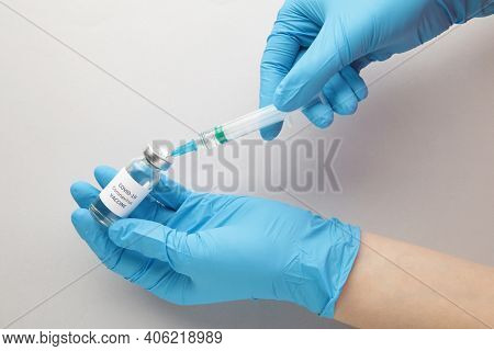 Bottle With Vaccine Against Covid 19 And Syringe In Hand Of Researcher Wearing Gloves On Grey Backgr