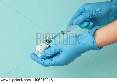 Bottle With Vaccine Against Covid 19 And Syringe In Hand Of Researcher Wearing Gloves On Blue Backgr