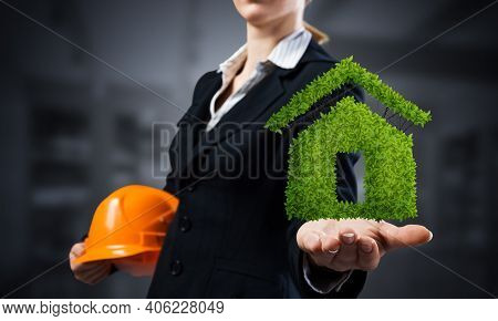 Real Estate Agent Holds In Palm Green Plant In Shape Of House. Woman In Business Suit With Safety He