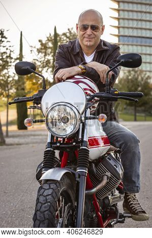 Man Sitting On A Motorcycle Smiling Cheerfully Posing On His Motorcycle Leaning On A Helmet. Safety 