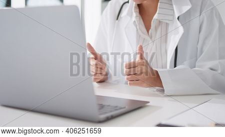 Asian Female Doctor Using Laptop Computer Online Video Call Remote Talking To Patient, Thumbs Up. Te