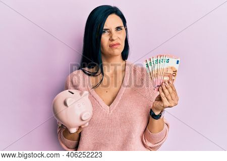 Young caucasian woman holding euro banknotes and piggy bank skeptic and nervous, frowning upset because of problem. negative person. 